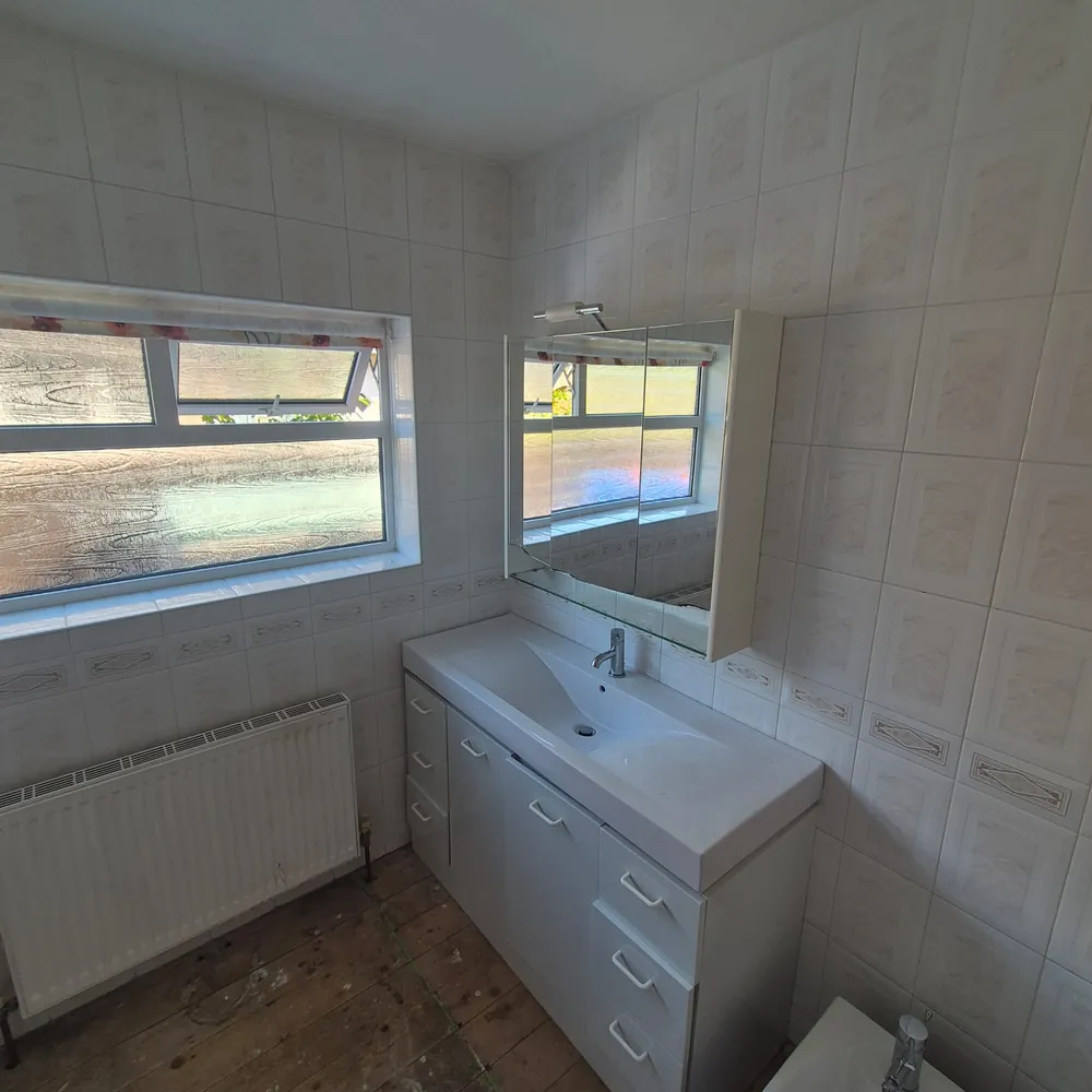 The old vanity wall with dated tiles and white cabinets