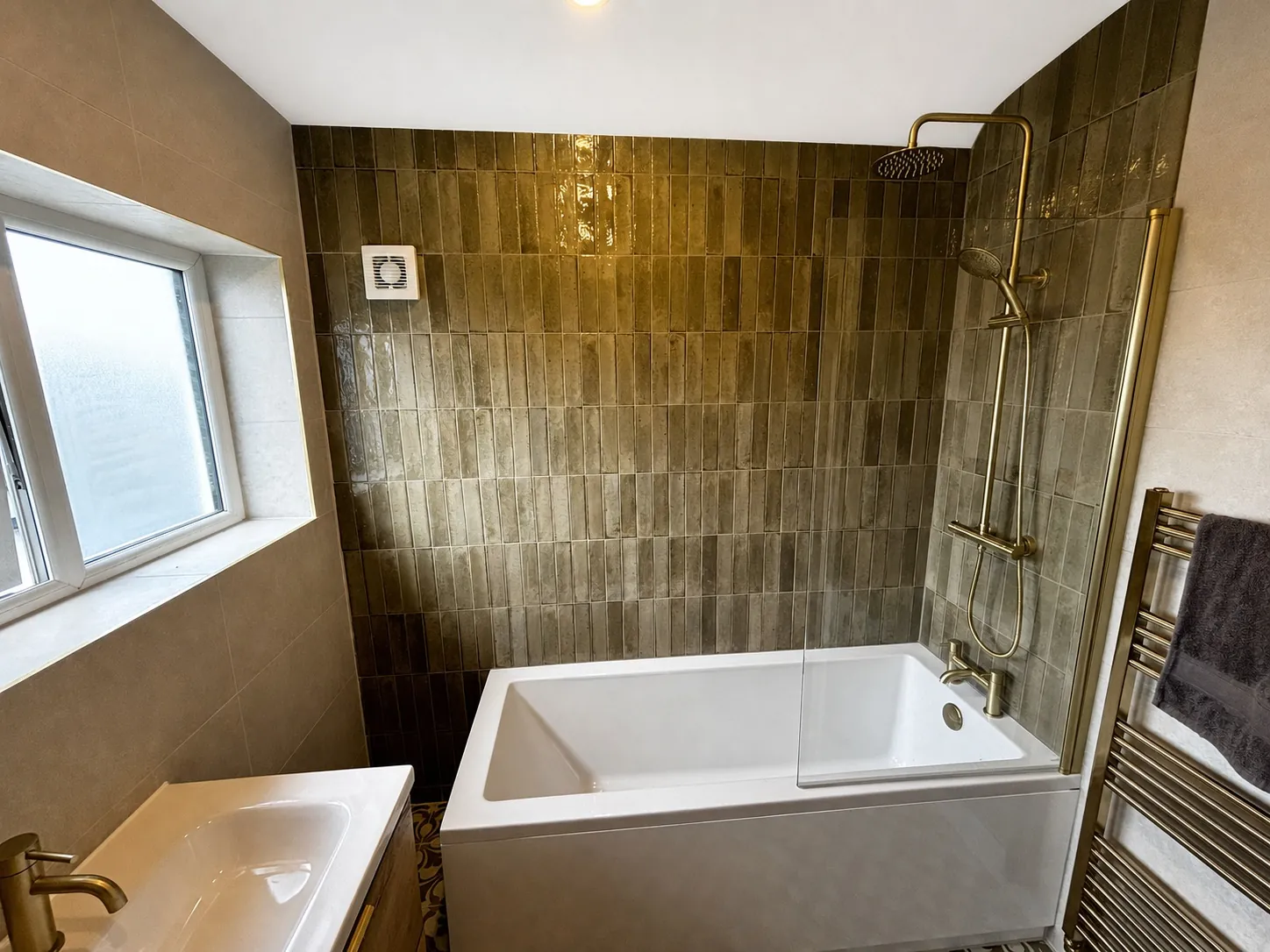 Olive tile bathroom with brass fittings and L-shaped bath