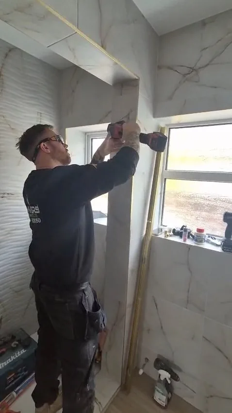 Mark, the owner of Danvers Northwest, tiling around a window on a marble bathroom job in branded workwear